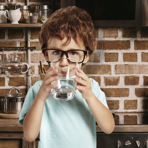 A boy drinking a glass of conditioned water treated by a Houston water softener company.