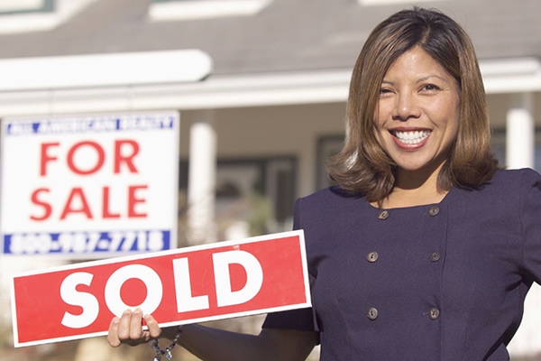 A real estate agent shows off a "SOLD" sign after selling a new home.