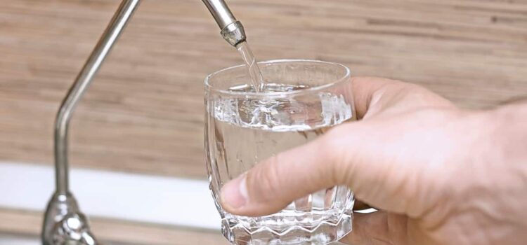 Person filling a glass with water from the Houston TX Water filtration system