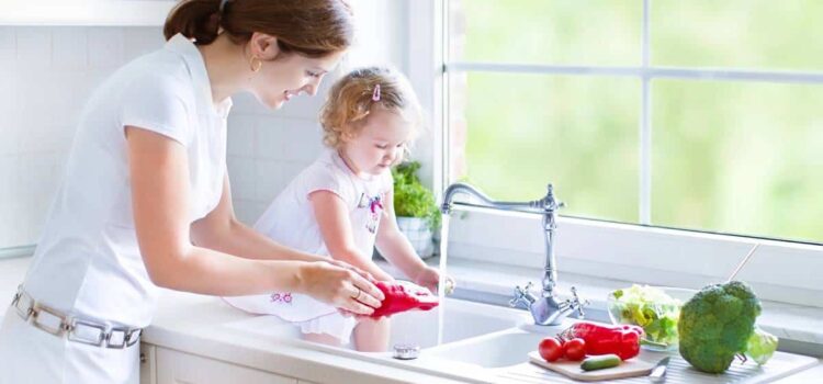 mother with her daughter in the kitchen washing some vegetables with clean water