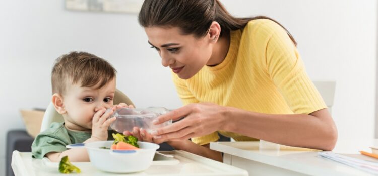 Toddler boy drinking filtered water near mother and food on high chair