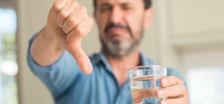 Man holding a glass of water giving a thumbs down, needing water softening in Katy.