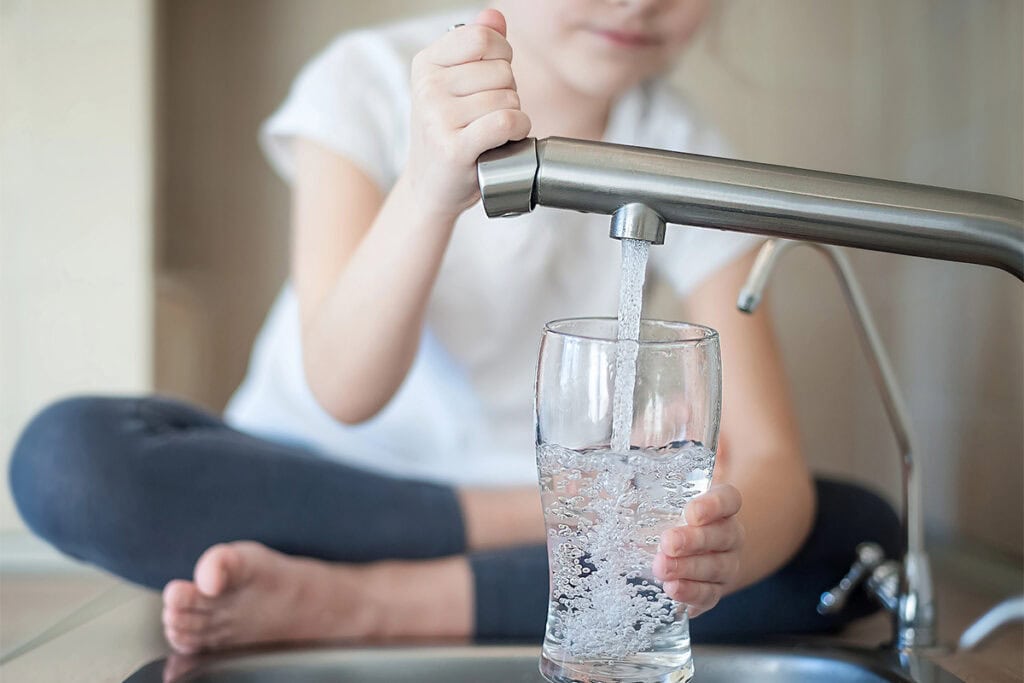 A girl is filling a glass with water from a kitchen sink tap.
