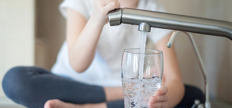 A girl is filling a glass with water from a kitchen sink tap.