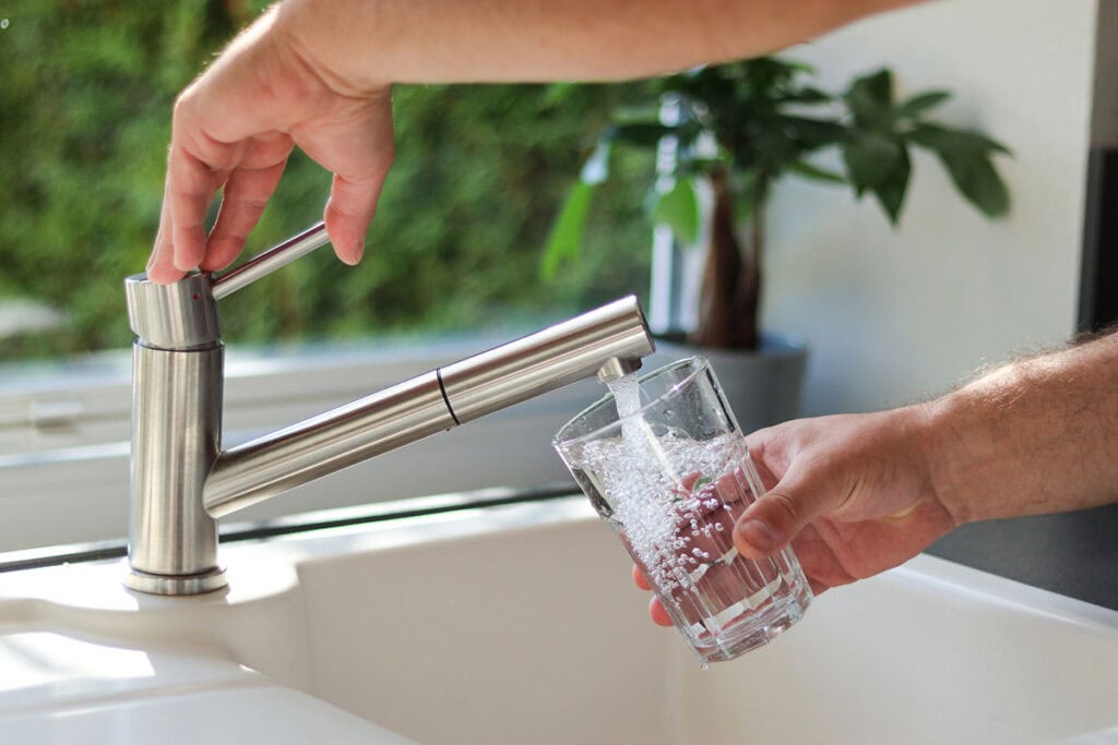 A man is pouring tap water into a glass.
